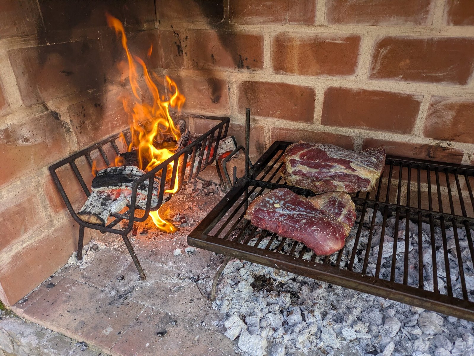 Asado tradicional argentino en preparación dentro de una parrilla de ladrillos. A la izquierda, un brasero de hierro con