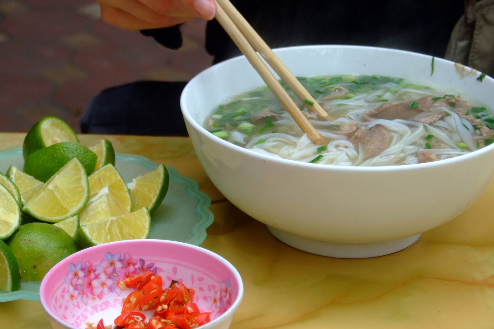 A steaming bowl of phở bò (rice noodle soup with beef) and its condiments, as served in the Cầu Giấy district, Hanoi.