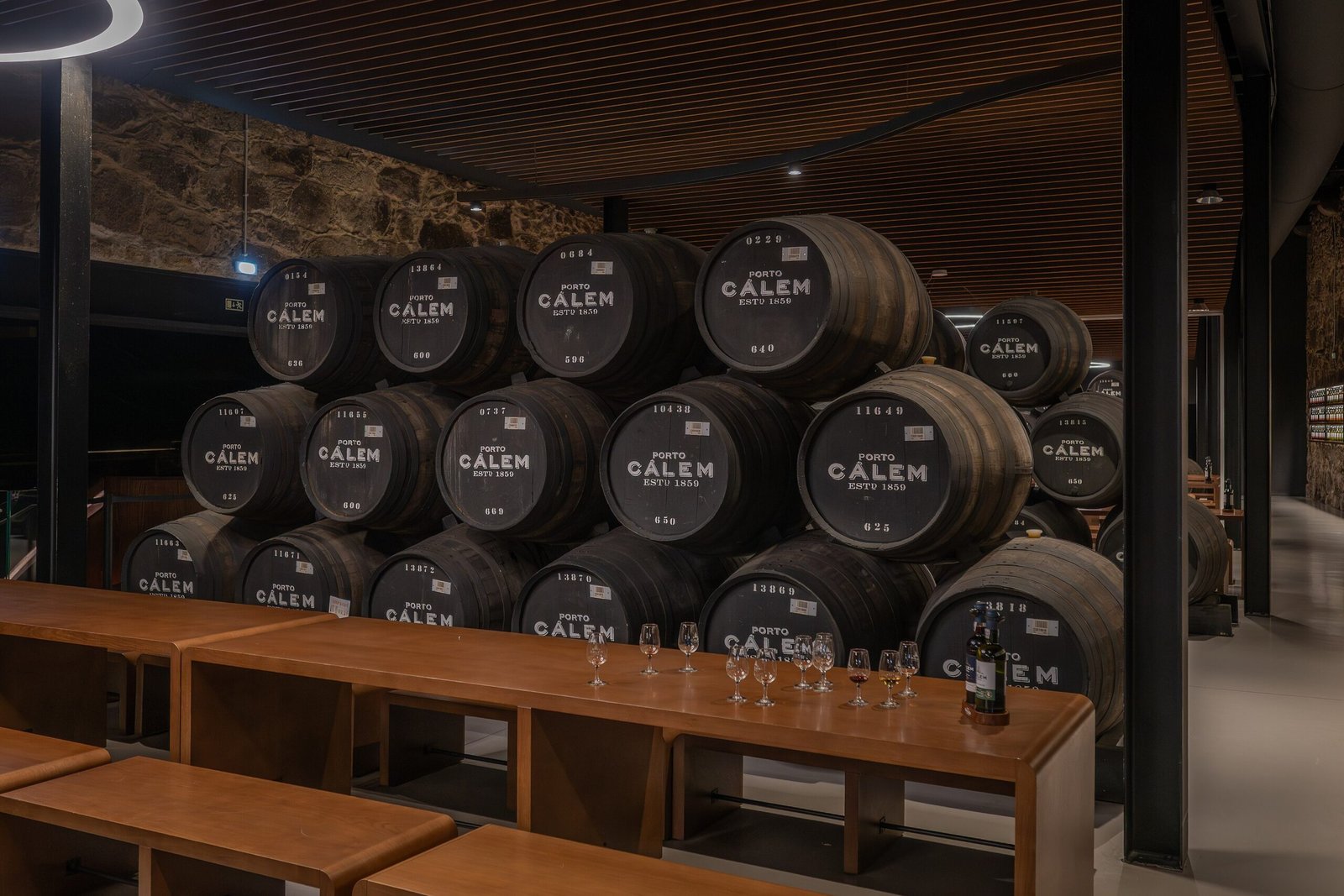A dimly lit, atmospheric cellar at Porto Calém, showcasing stacks of large, traditional wooden barrels. The barrels, pre